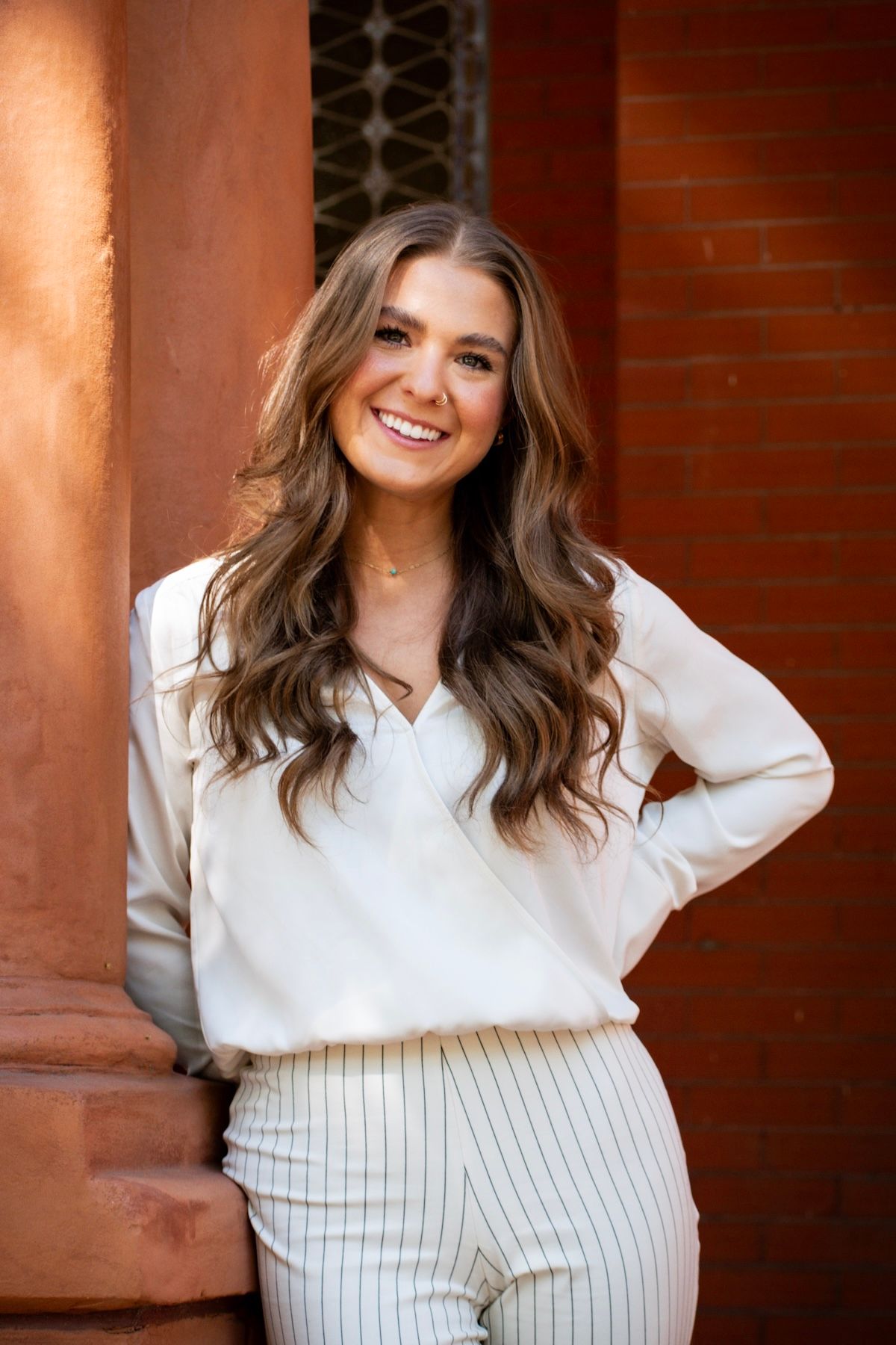 Man in blazer leaning on a railing smiling. Brick building in the background.