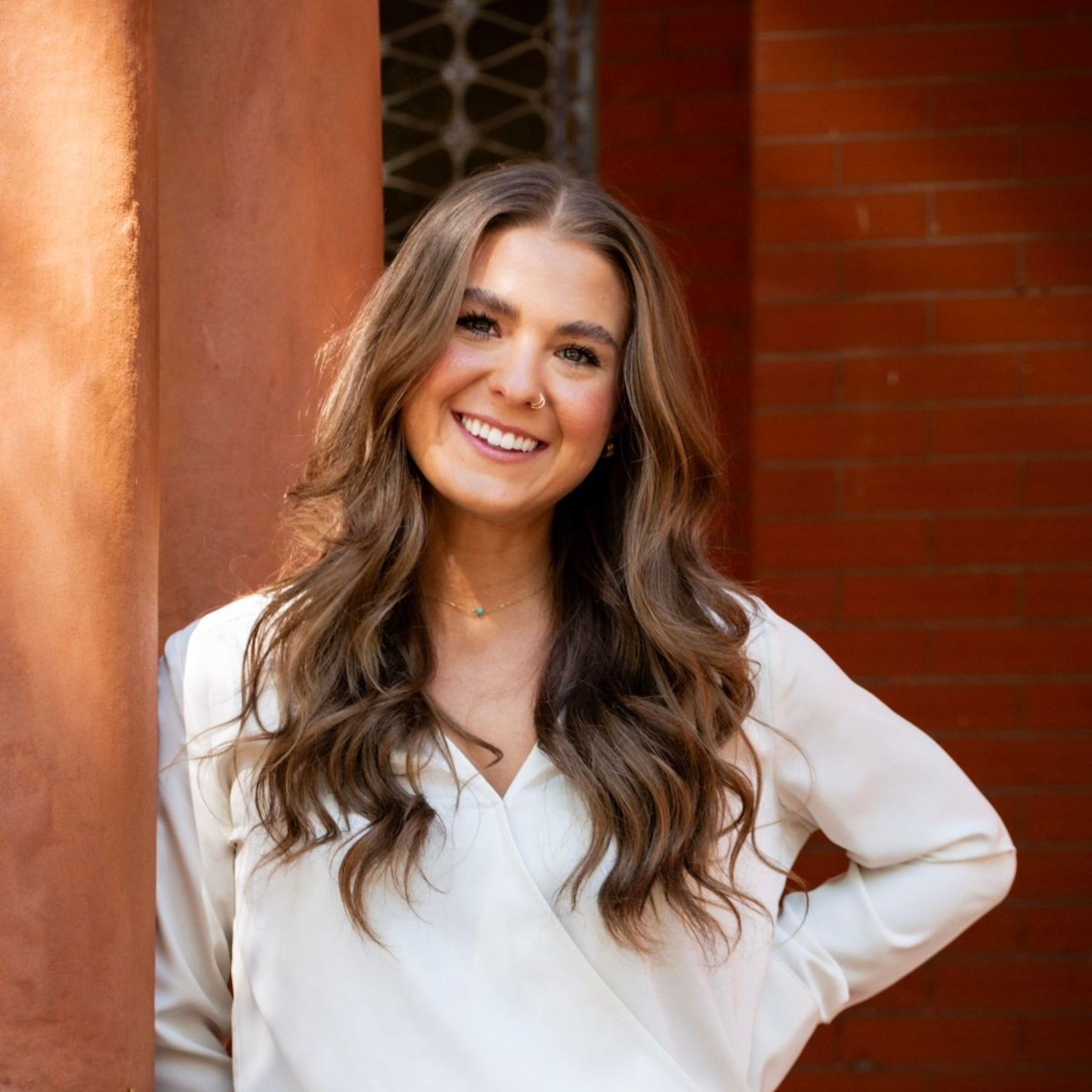 Man in tweed jacket leans on railing, smiling outdoors near steps and trees.