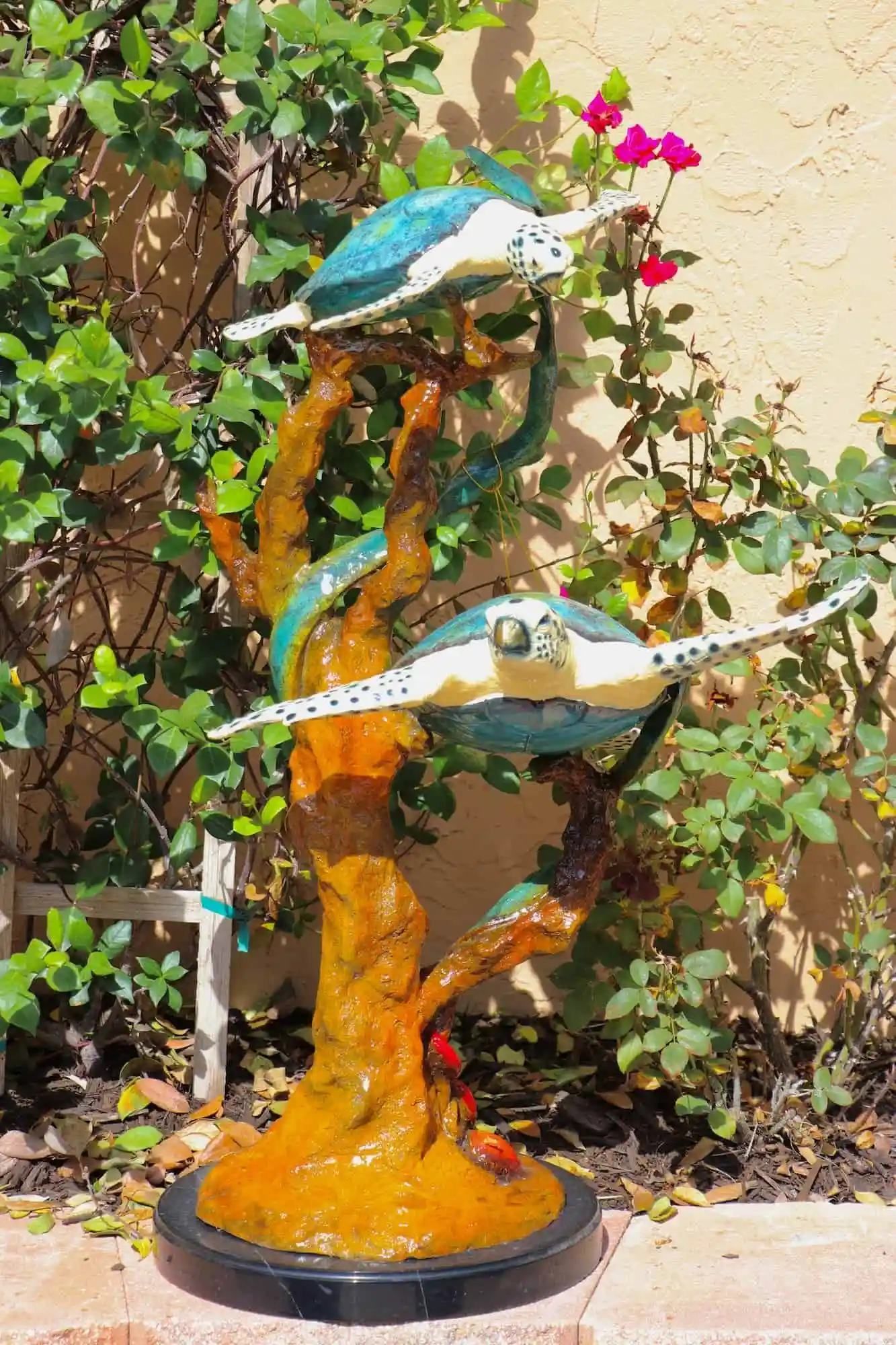 Sculpture of two turtles, one above the other, with aqua and white shells, perched on a brown, twisting tree trunk base.