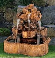 A tiered outdoor fountain made of brown stone. Water flows from the top, cascading into the lower basins.