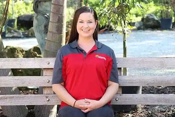 Woman in red and gray polo shirt smiles while sitting on a wooden bench outdoors.