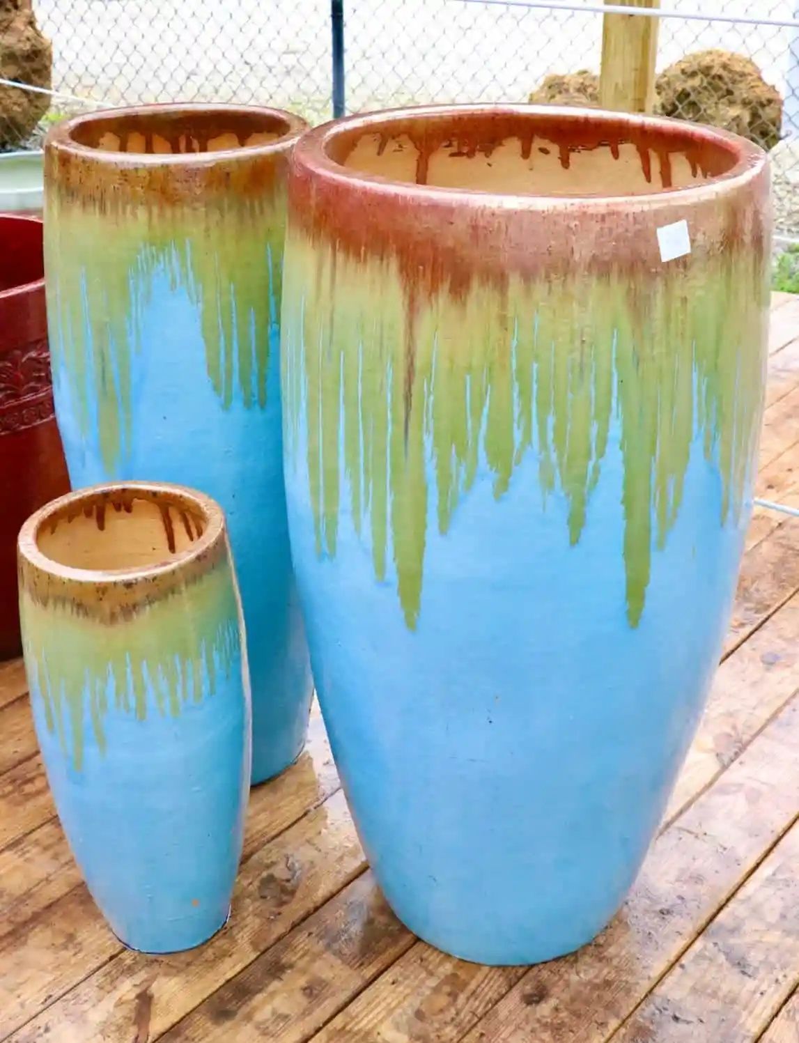 Three tall, glazed ceramic planters with a blue base and brown, green, and gold drip glaze. They are on a wooden surface.
