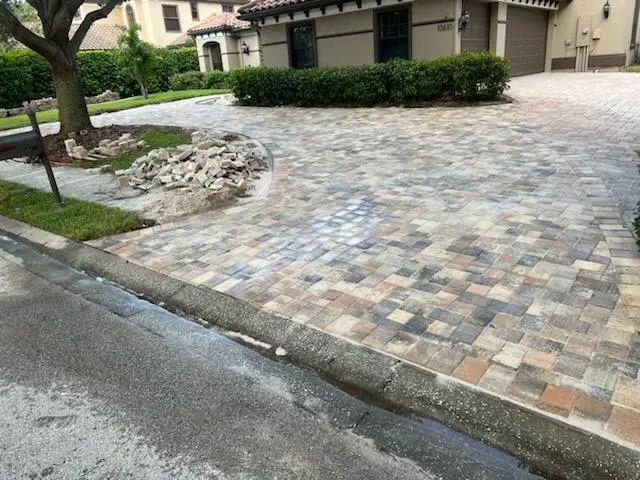 Paver driveway in front of a house. Multi-colored pavers lead to a garage. The driveway curves towards a small rock feature.
