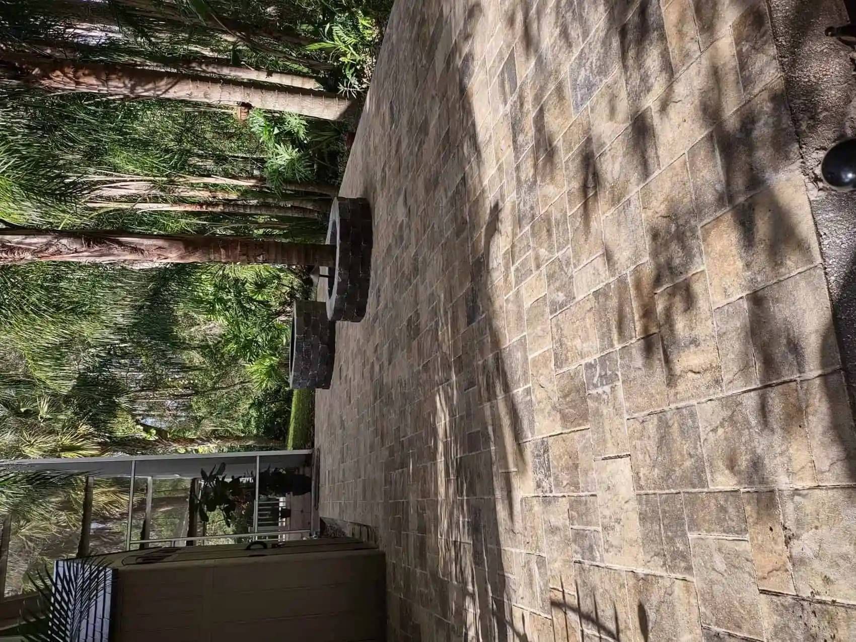 A brick patio with two stone wall features, set in a forest environment. The scene is bathed in sunlight.