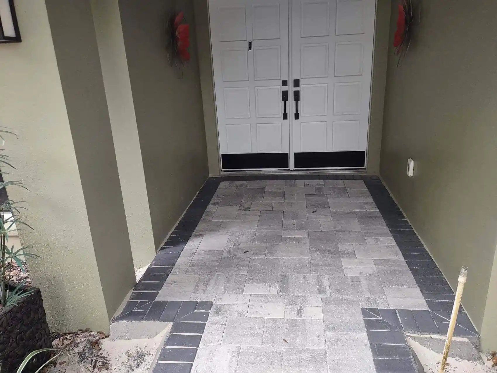 Entrance of a building with a gray paved walkway leading to white double doors. Dark gray trim surrounds the walkway.