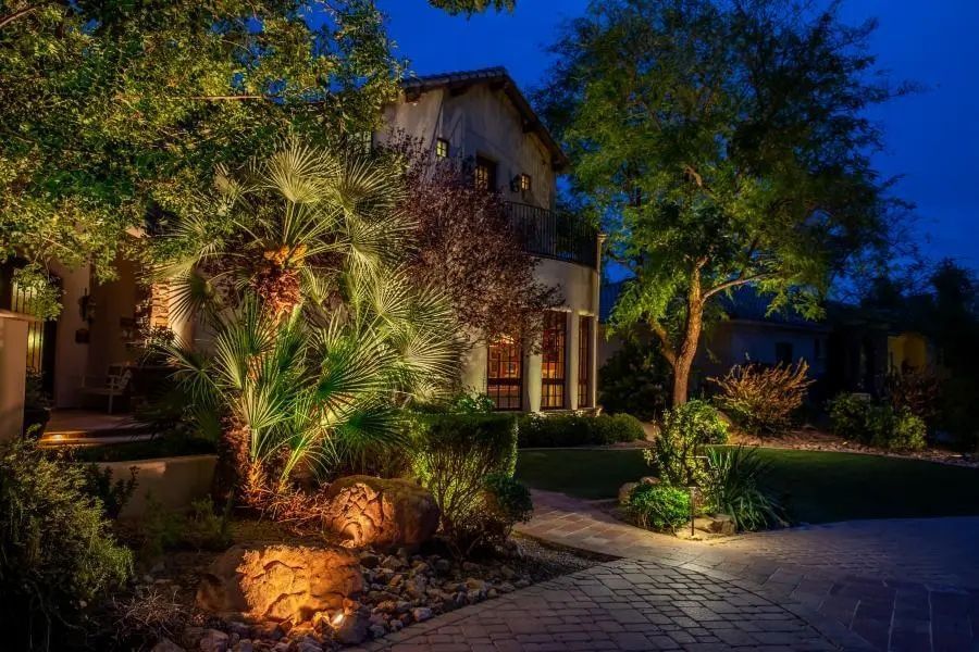 House at night with landscape lighting illuminating trees and path.