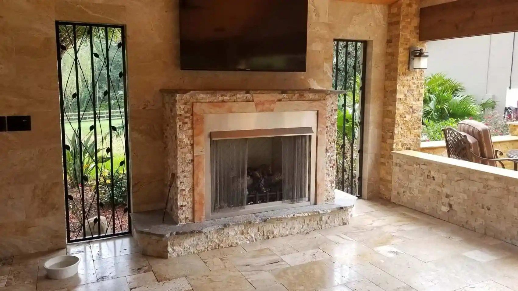 Outdoor fireplace with stone surround and built-in television. Wrought iron decorative screens flank the fireplace.