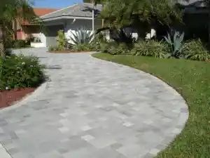 Driveway made of gray pavers leading to a house with green lawn on the side.