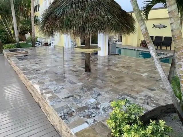 Patio with stone pavers, pool, and tiki umbrella. A house is in the background.