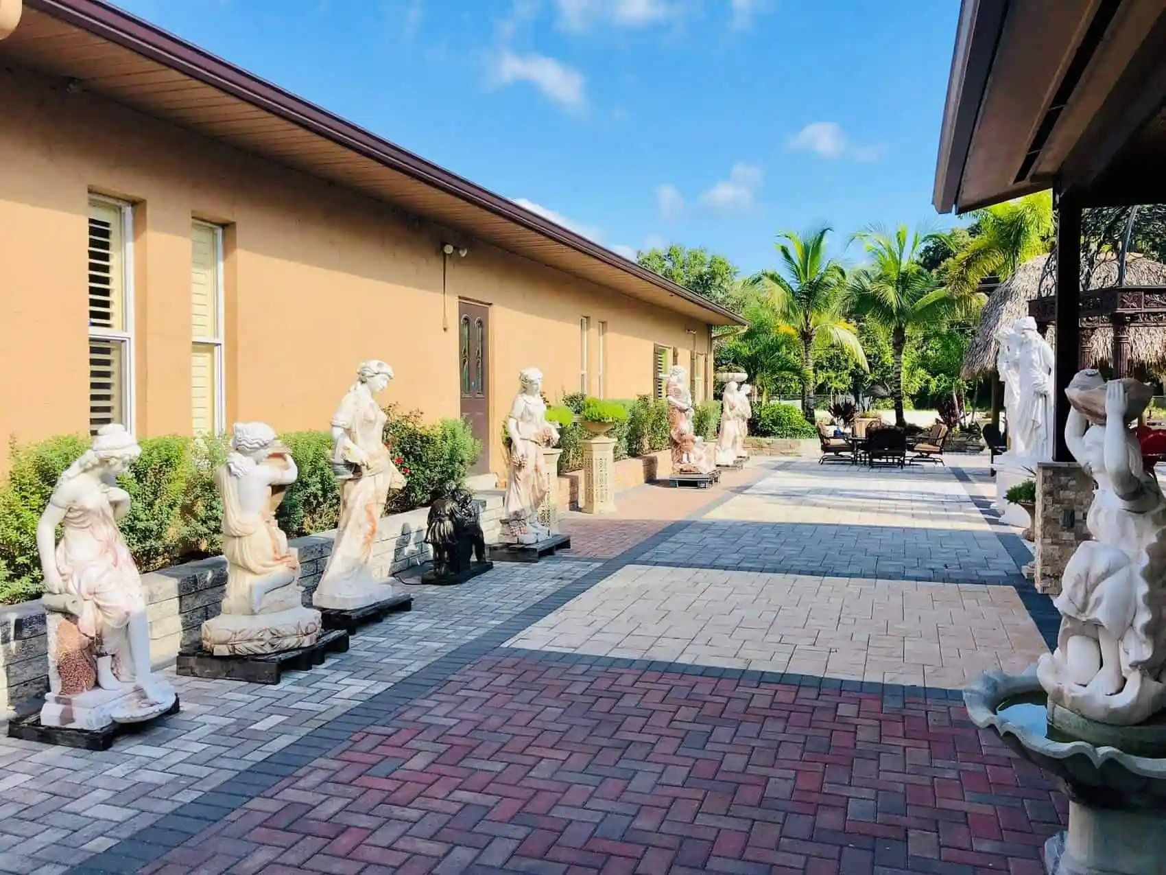 A pathway lined with statues of women outside a tan building, under a blue sky.