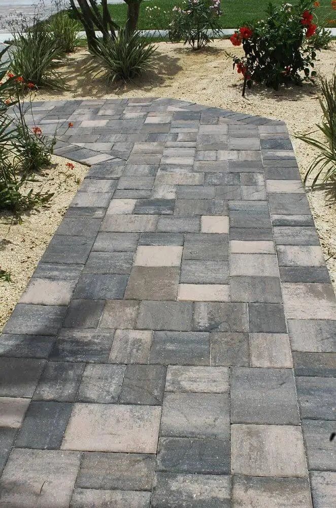 A paved pathway of gray and tan blocks winds through a landscaped garden.