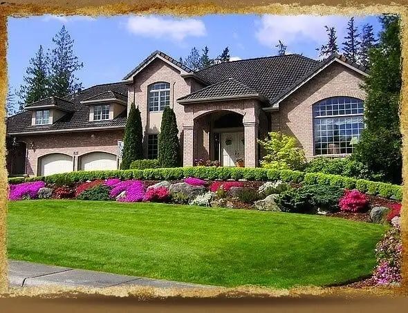 House with a well-manicured lawn and colorful flowerbeds under a bright blue sky.
