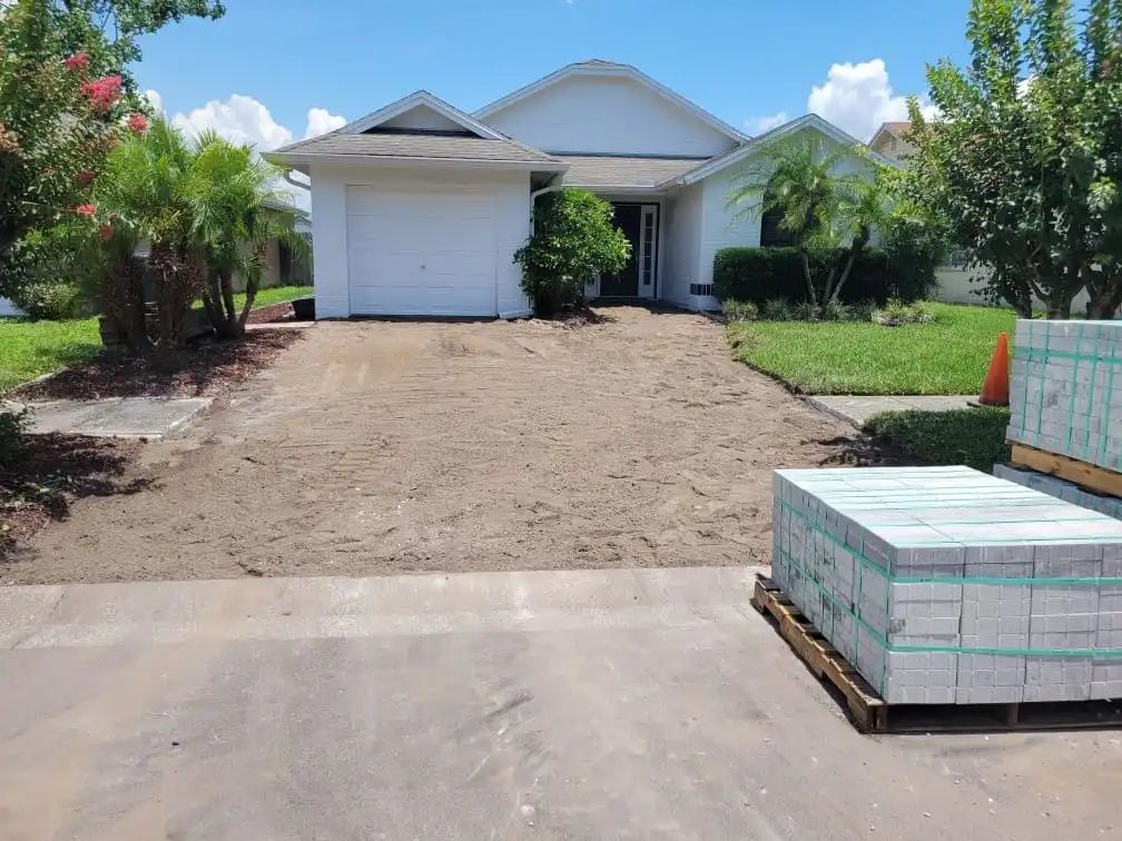 Driveway renovation: A home with a dirt-covered driveway. Pallets of paving stones sit on the right.