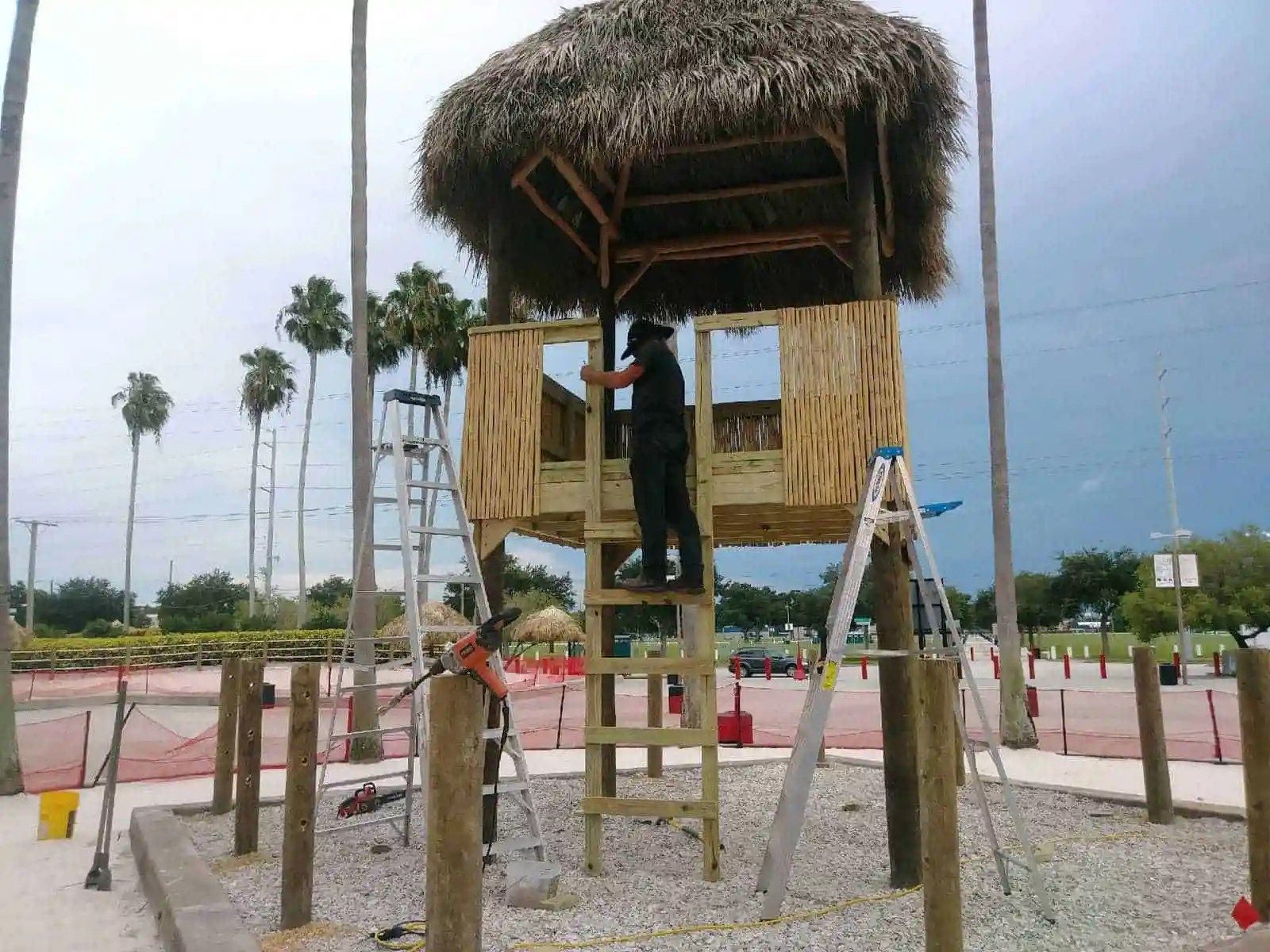 Construction of a two-story wooden structure with a thatched roof, likely a treehouse, with workers on ladders.