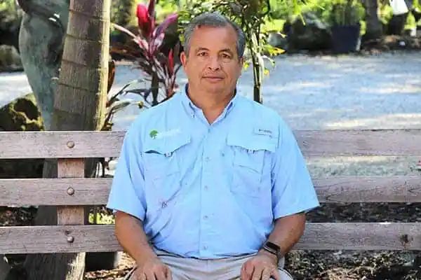 Man sitting on a wooden bench in a garden, wearing a light blue shirt.