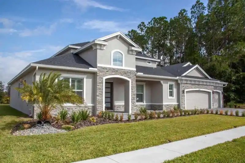 A modern, light gray two-story house with stone accents, a manicured lawn, and a driveway.
