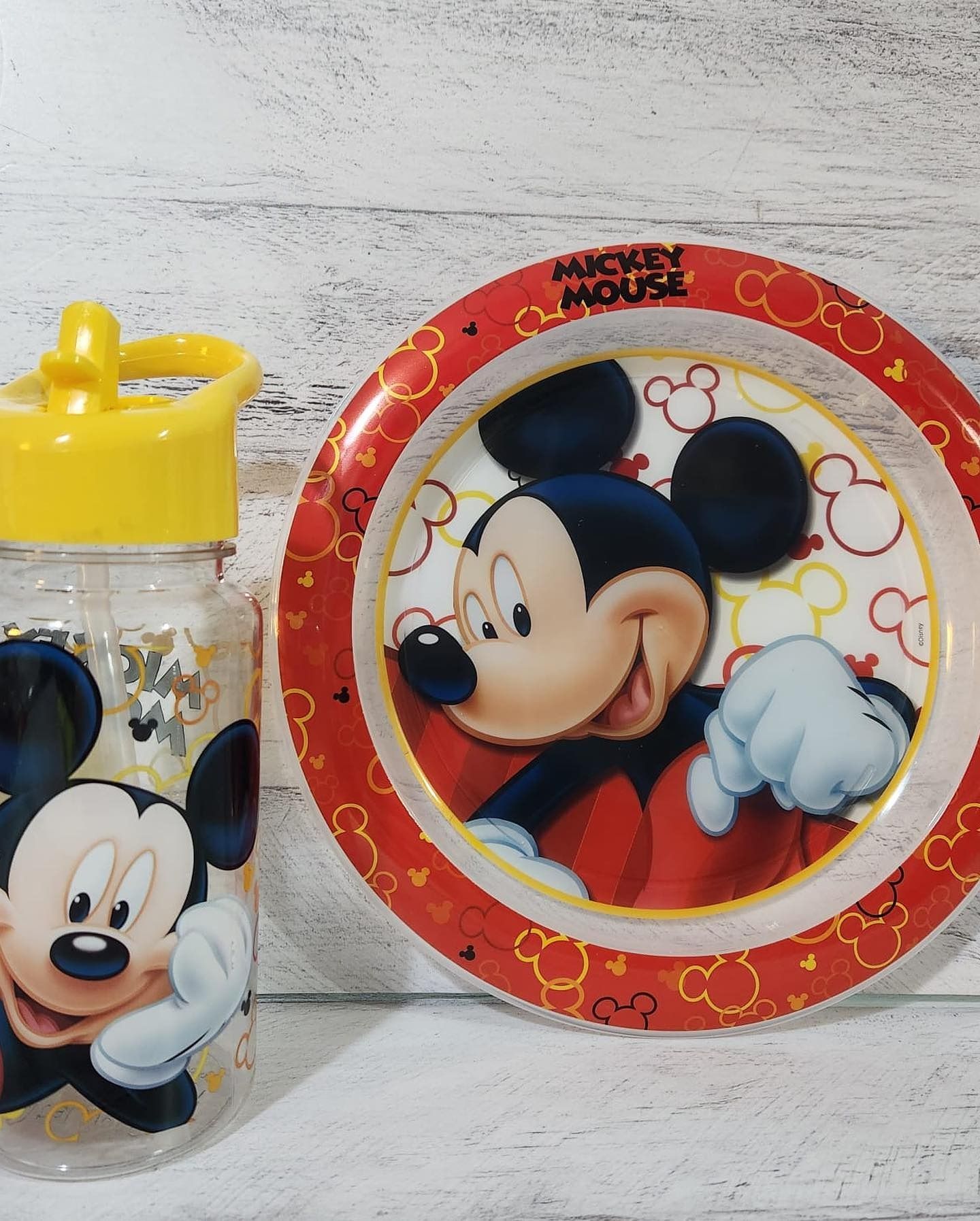 Botella de agua y plato de Mickey Mouse. El plato presenta a Mickey con un borde rojo. La botella tiene un tapón amarillo.