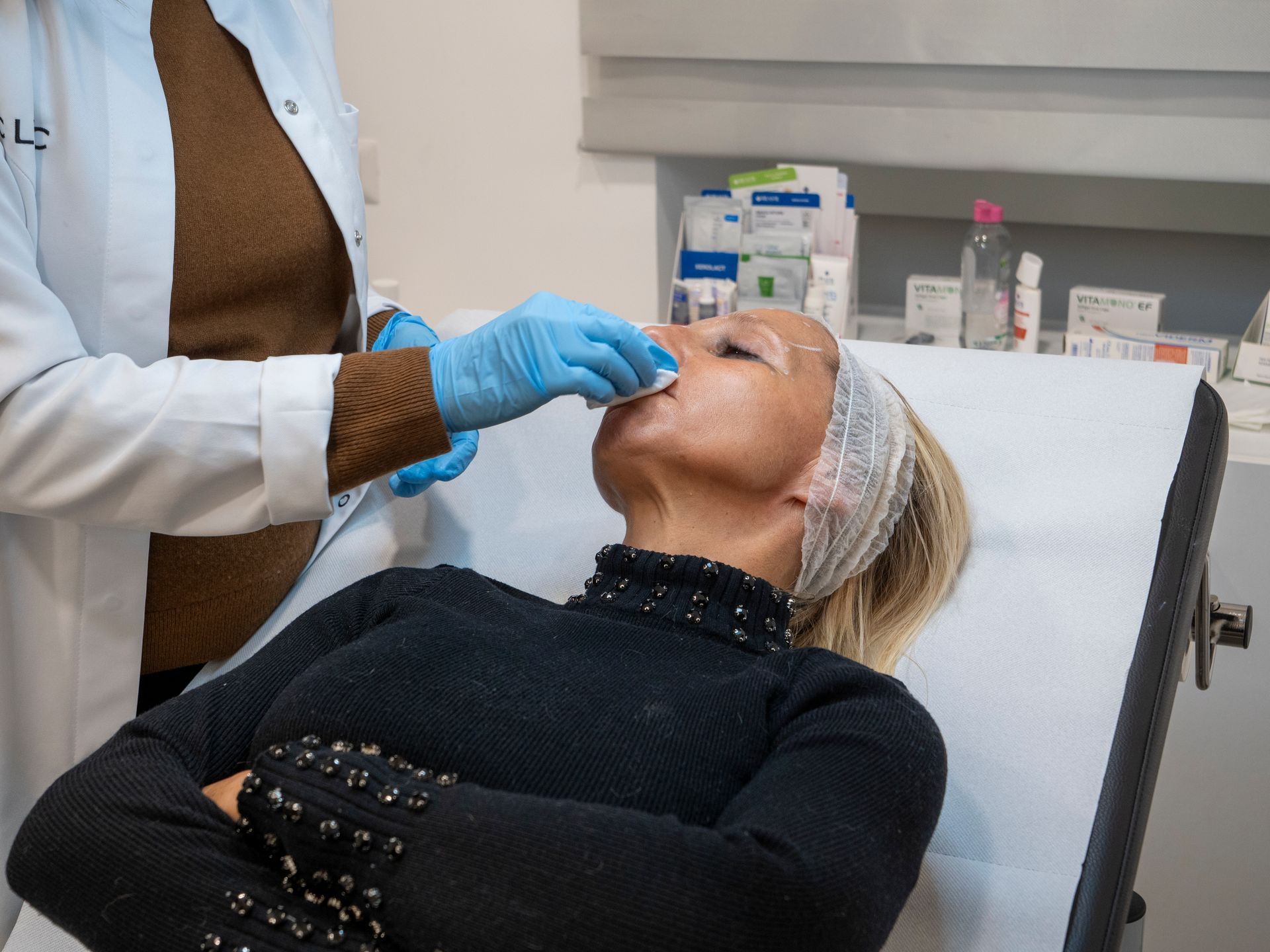 Una donna è sdraiata su un letto mentre un medico si sottopone a un trattamento per il viso.