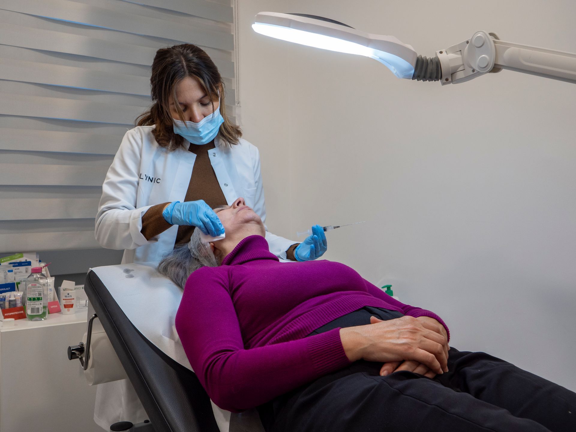 Una donna è sdraiata su un letto mentre un medico si sottopone a un trattamento per il viso.