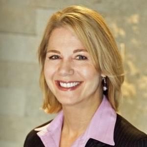 A woman in a suit and a pink shirt is smiling for the camera