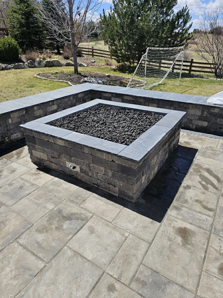 A fire pit is sitting on top of a patio next to a fence.