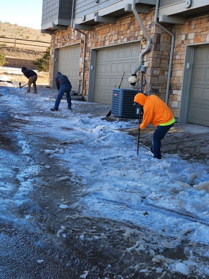 Three men are shoveling snow in front of a building