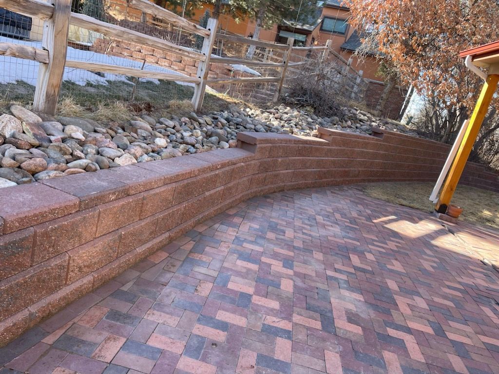 A brick walkway with a stone wall and a wooden fence in the background.