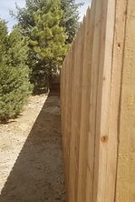 A wooden fence along a dirt path with trees in the background.