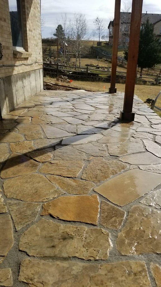 A stone patio with a wooden pergola and a house in the background.