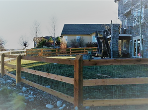 A wooden fence surrounds a lush green yard in front of a house.