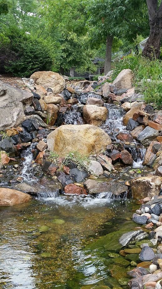 A small waterfall is surrounded by rocks and trees in a park.