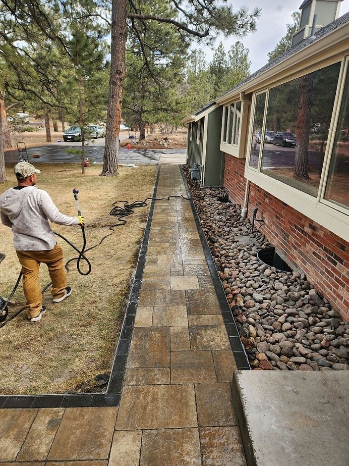 A man is spraying water on a sidewalk in front of a house.