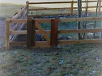 A wooden fence with a gate in the middle of a grassy field.