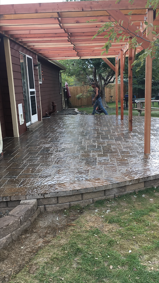 A man is standing on a patio under a pergola in front of a house.