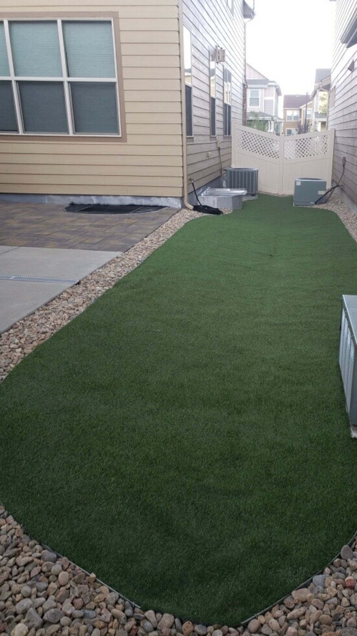 A backyard with a lot of grass and rocks in front of a house.