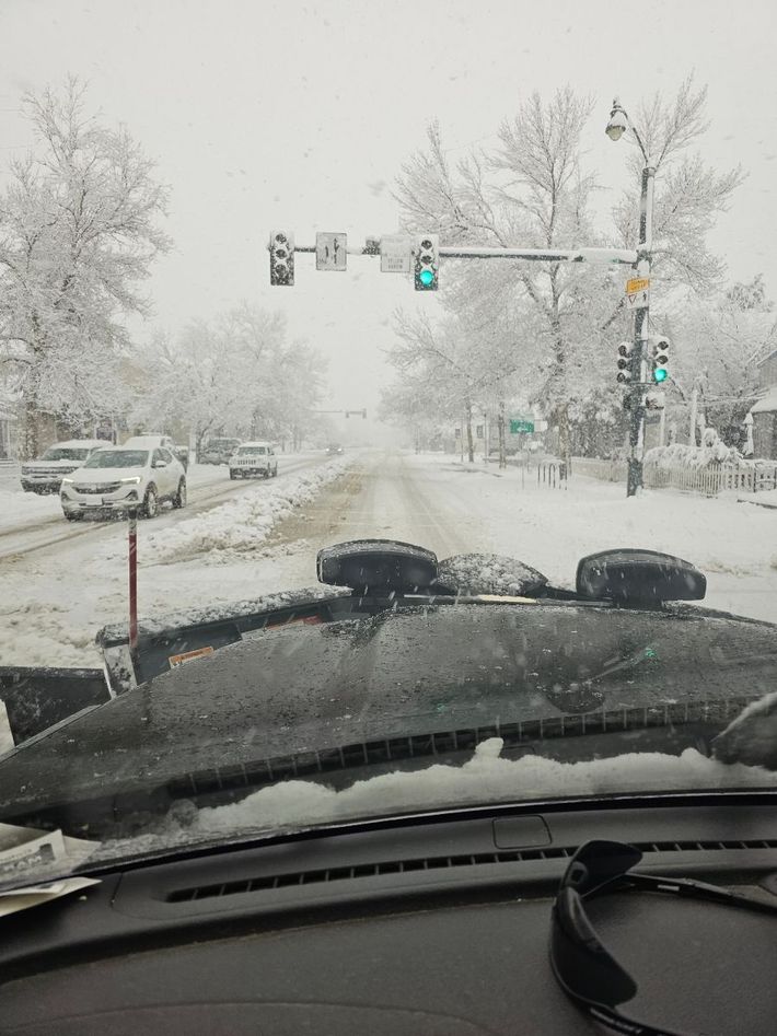 A snowy street is visible through the windshield of a car.