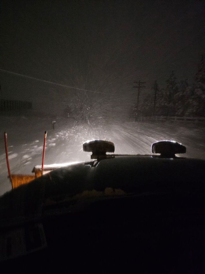 A snow plow is driving down a snowy road at night.