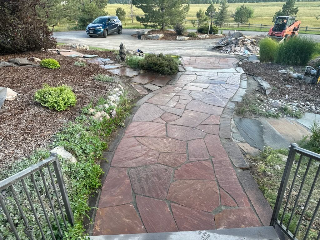 Stone pathway leading up to a house with a car and construction equipment in the background.