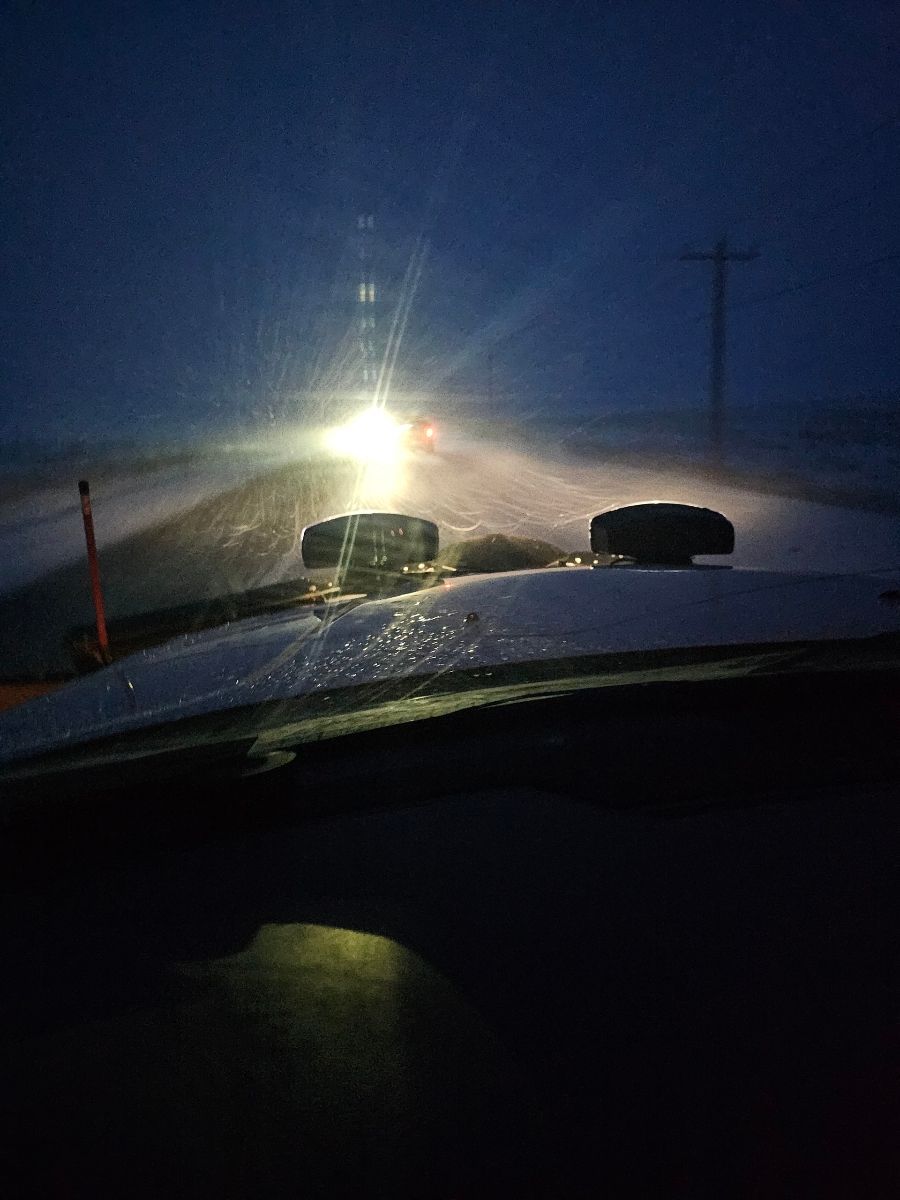 A car is driving down a snowy road at night.