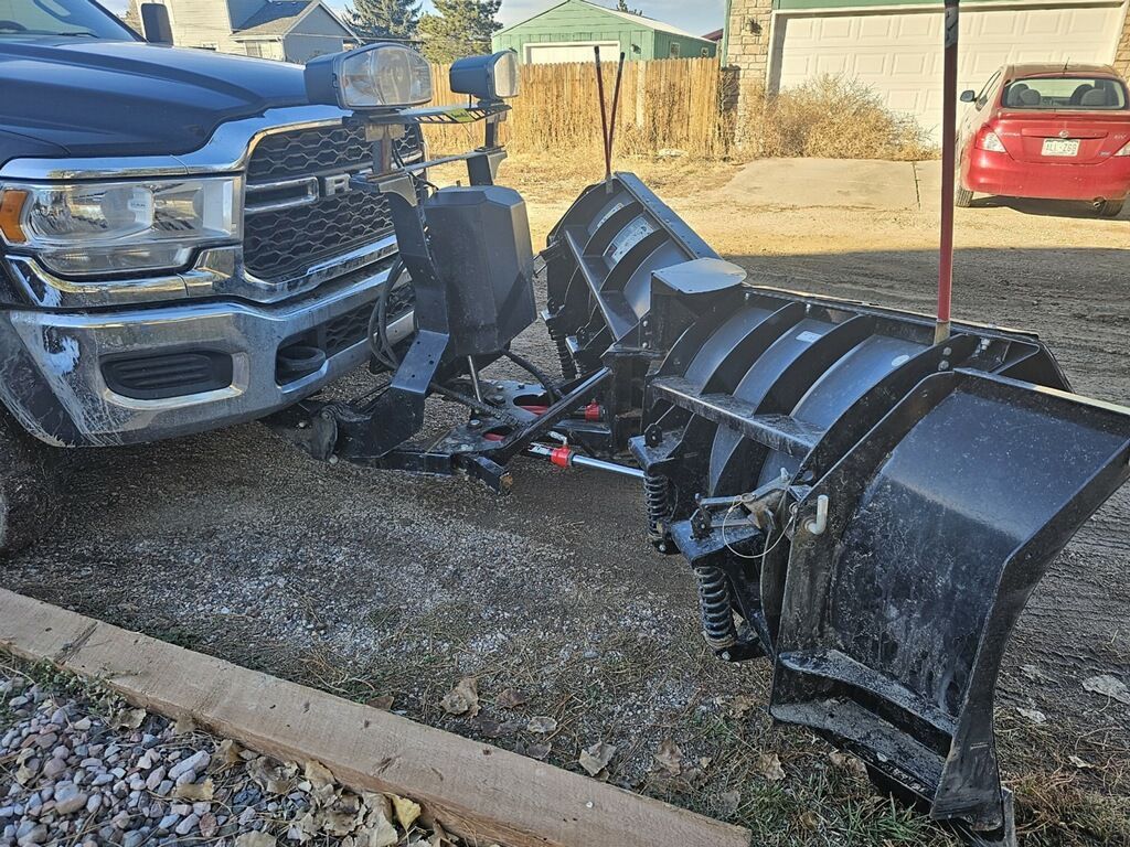 A truck with a snow plow attached to it is parked in a gravel lot