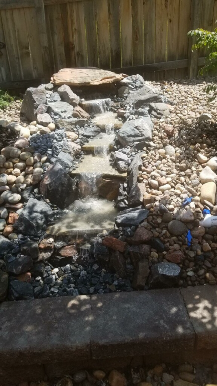 A small waterfall is surrounded by rocks and a wooden fence