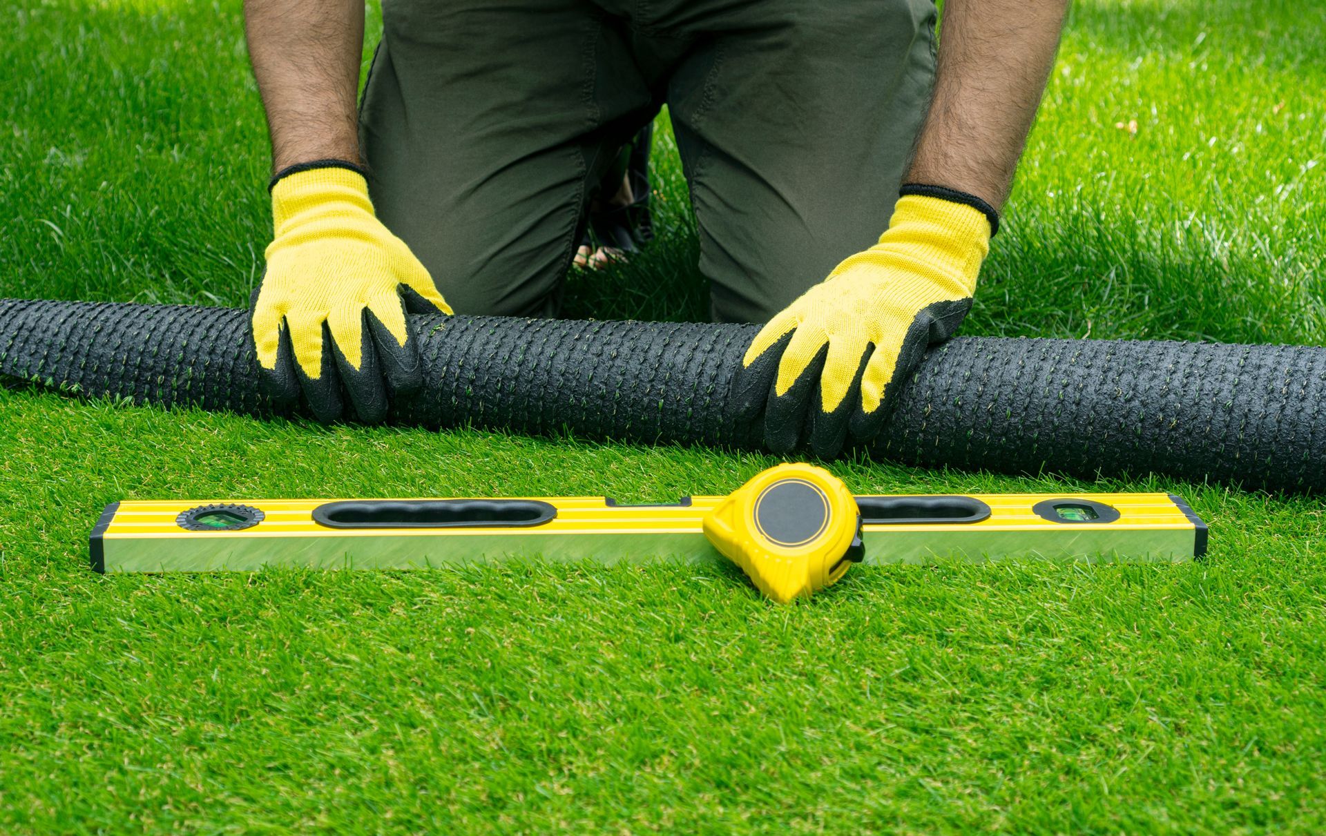 A man is kneeling on the grass with a tape measure and a level.