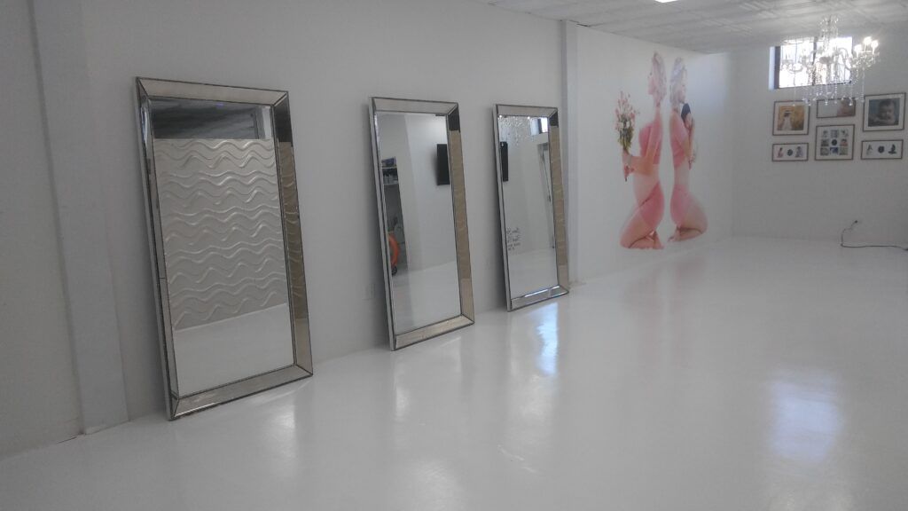 Three mirrors are lined up in a white room with glossy floor.