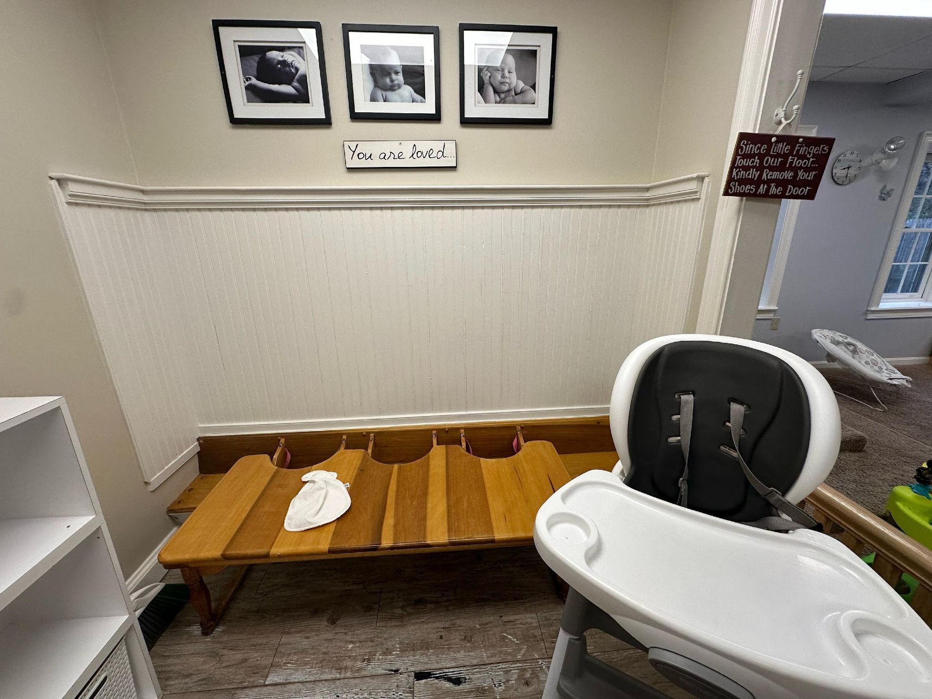 A brightly lit nursery area featuring a wooden bench, a baby high chair, and wall art.
