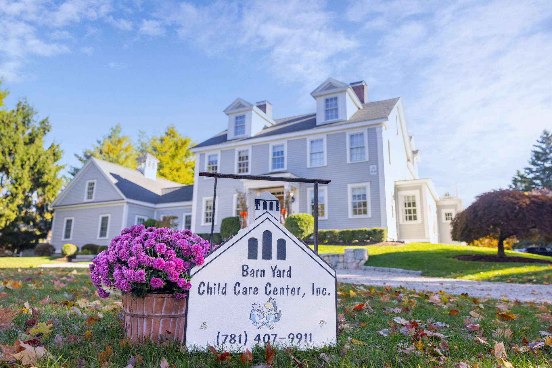 A blue child care center building with a sign in the foreground, next to a pot of purple flowers on a sunny day.