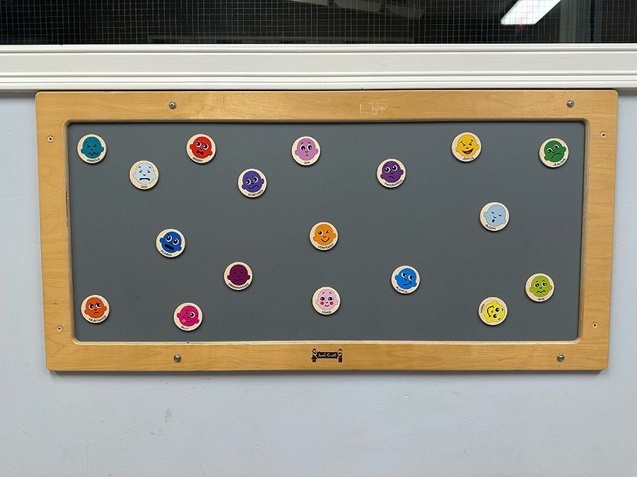 A wall-mounted magnetic board displays various colorful icons showing different facial expressions of emotion.
