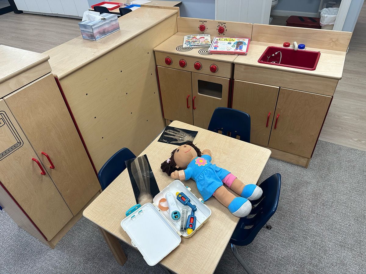 A toy kitchen and a table with a doll and medical kit for pretend play.