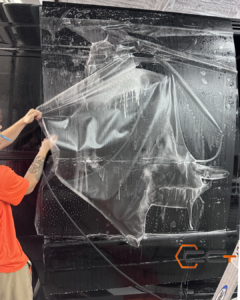 A man is wrapping a black van with clear plastic