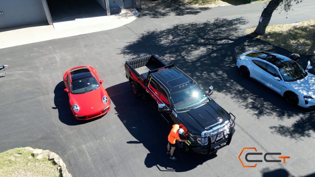 A red car is parked next to a black truck and a white car