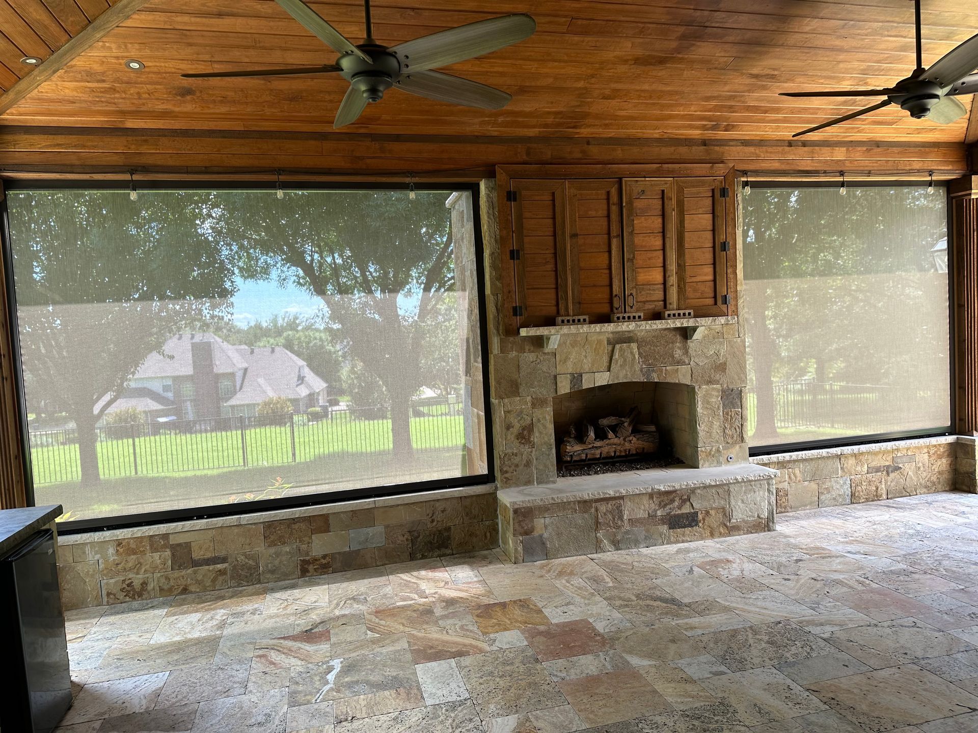 A screened in porch with a fireplace and a ceiling fan.